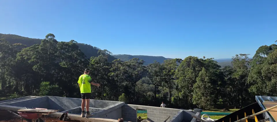 Worker screeding a slab on an elevated hillside site with forested valley views behind