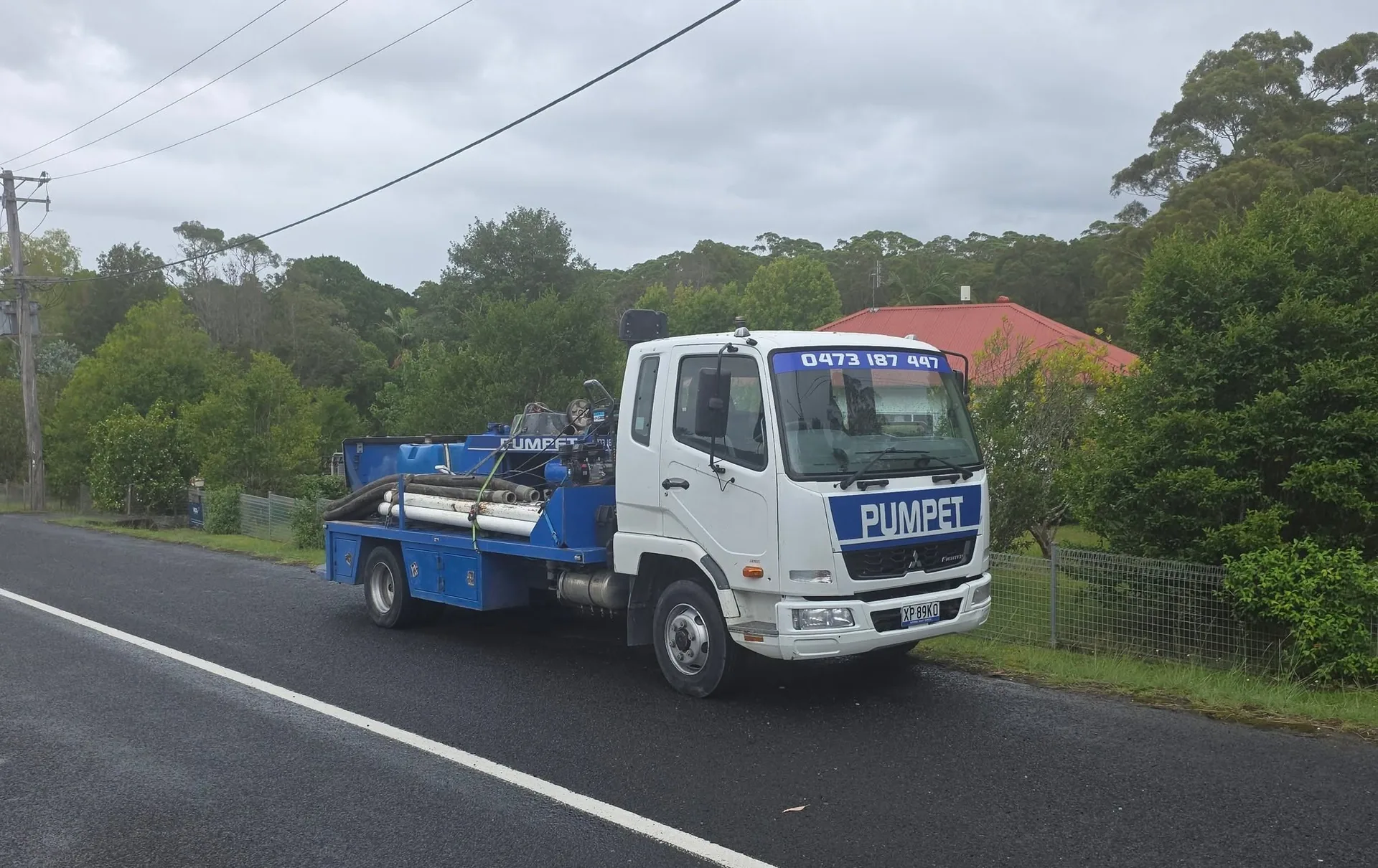 Pumpet truck travelling a rural road past residential properties