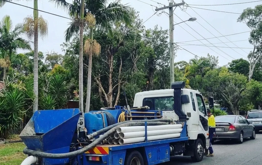 Pumpet truck parked on a palm-lined suburban street with hose and pipes loaded on the tray