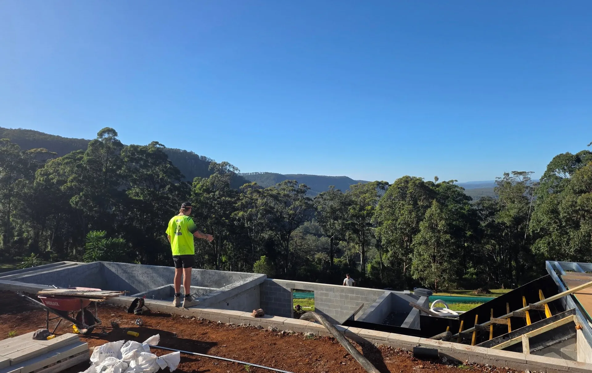 Worker screeding a slab on an elevated hillside site with forested valley views behind